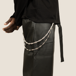 ICED London: close-up of black top and leather pants with layered silver chain accessory draped from the waistband (side view).