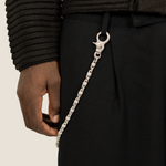 ICED London silver chain clipped to black trousers via belt loop, close-up of crescent clasp and linked chain.